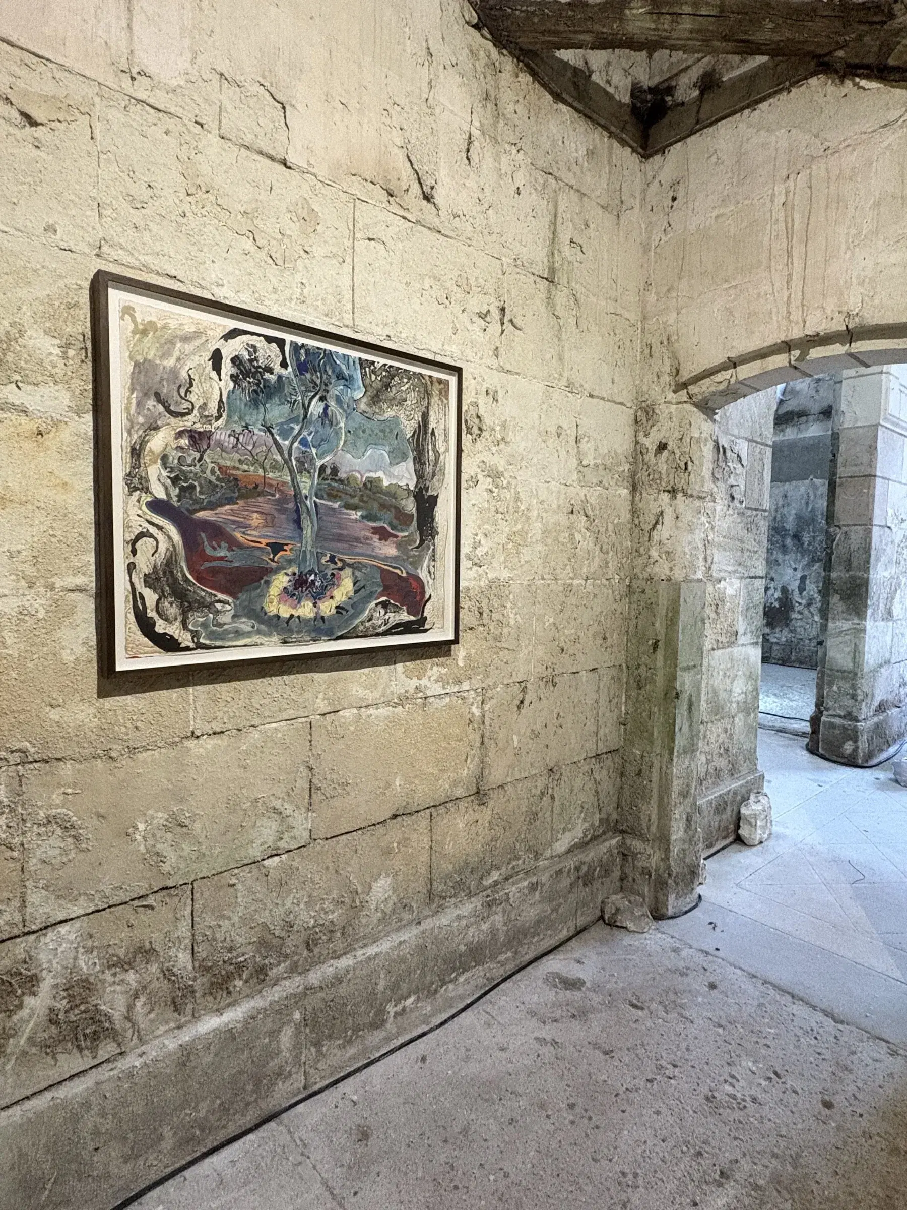 Framed mixed-media work installed at the junction of two stone galleries.