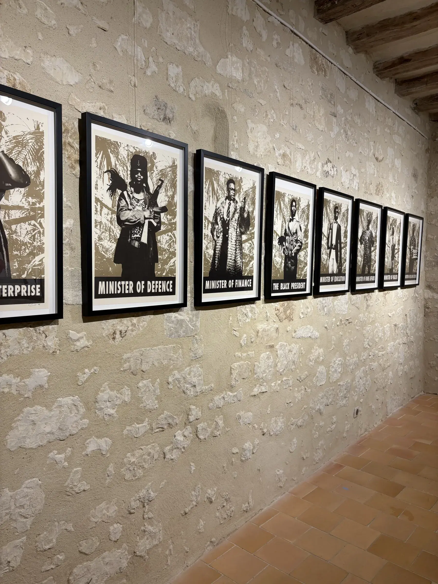 A row of framed black-and-white political portraits installed along a rough stone wall.