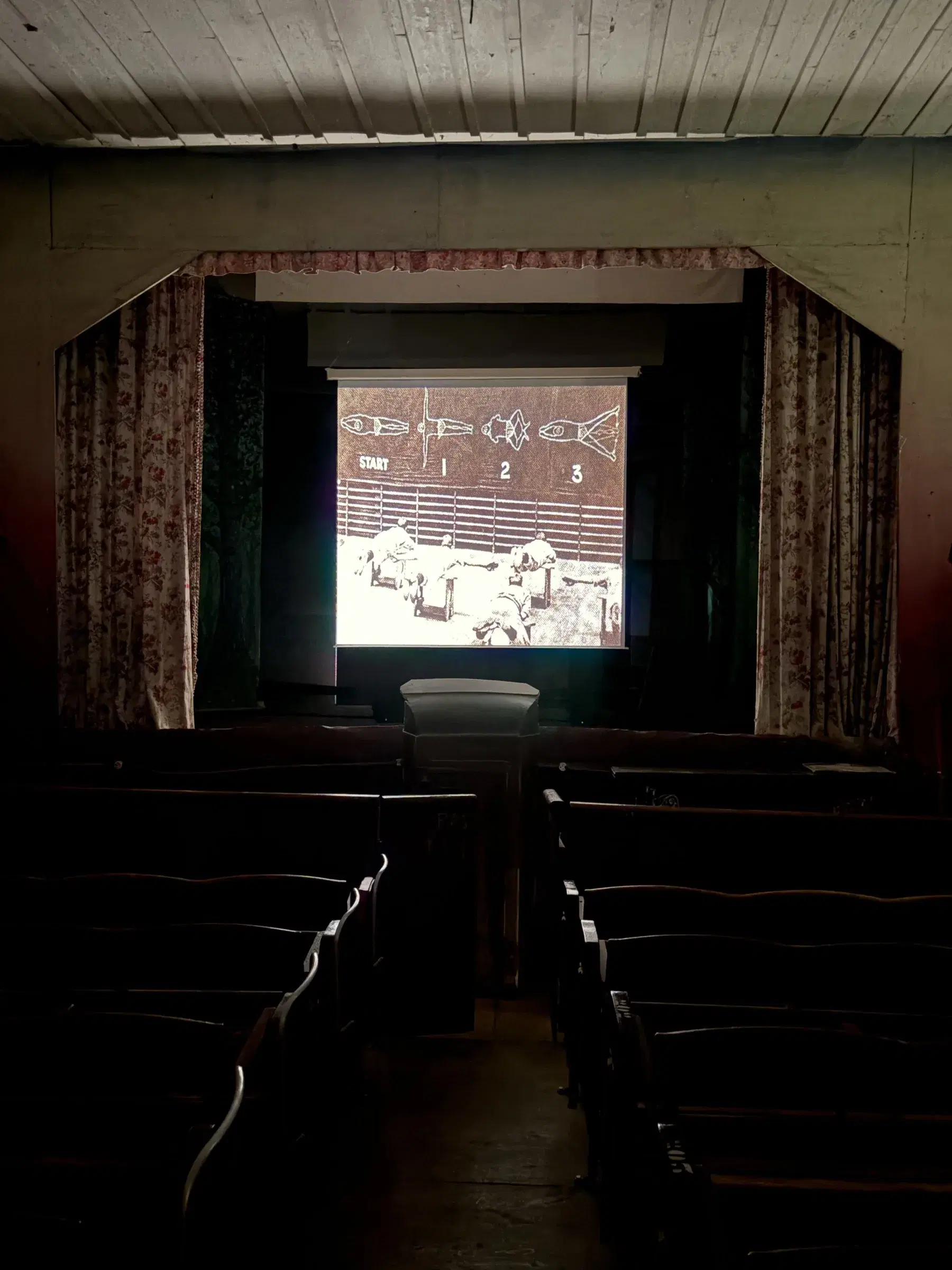 Film projection seen from the back of the wooden theatre auditorium.