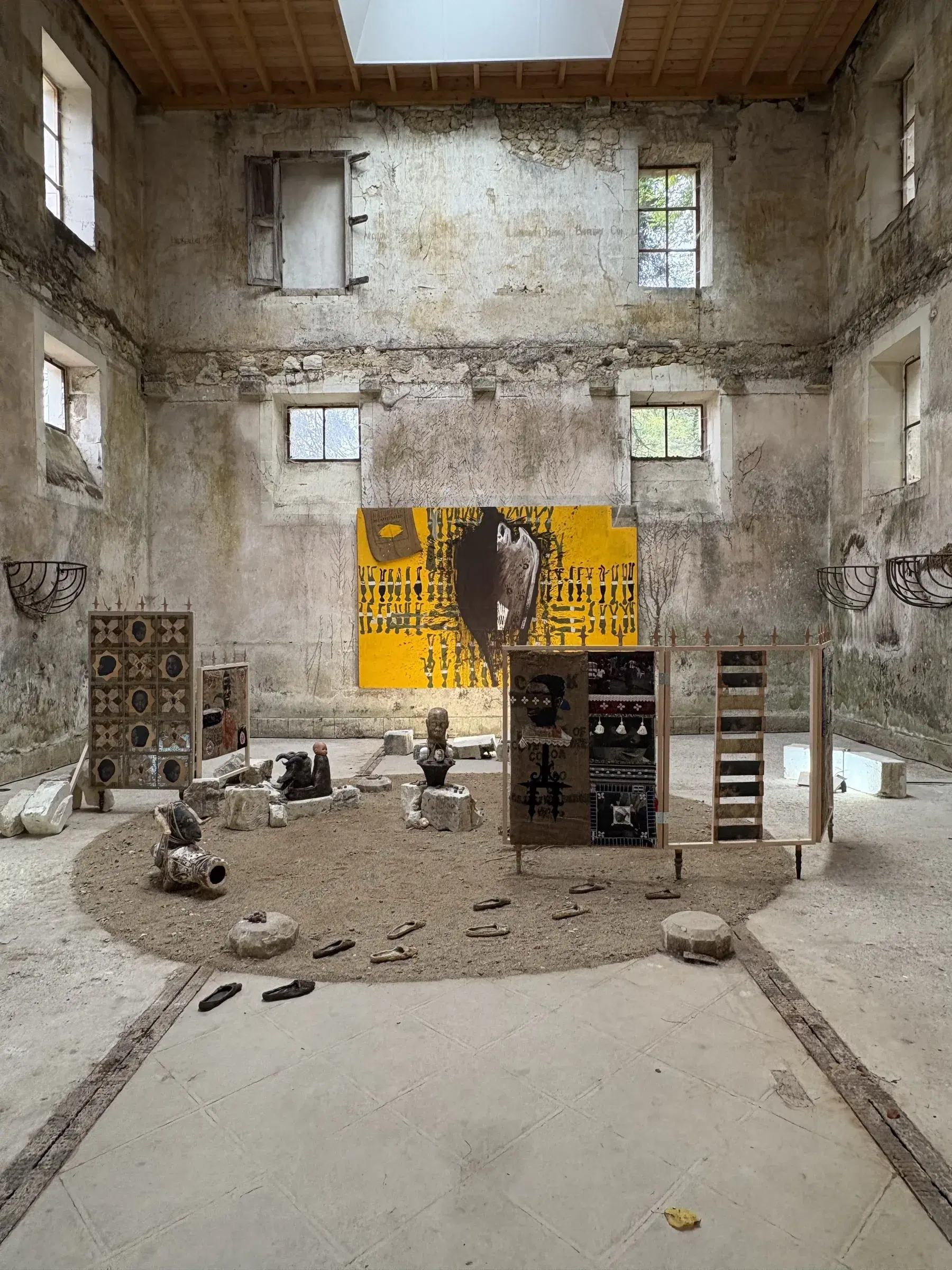 Wide installation view with sculptures and large works arranged around the central floor of the former stables.