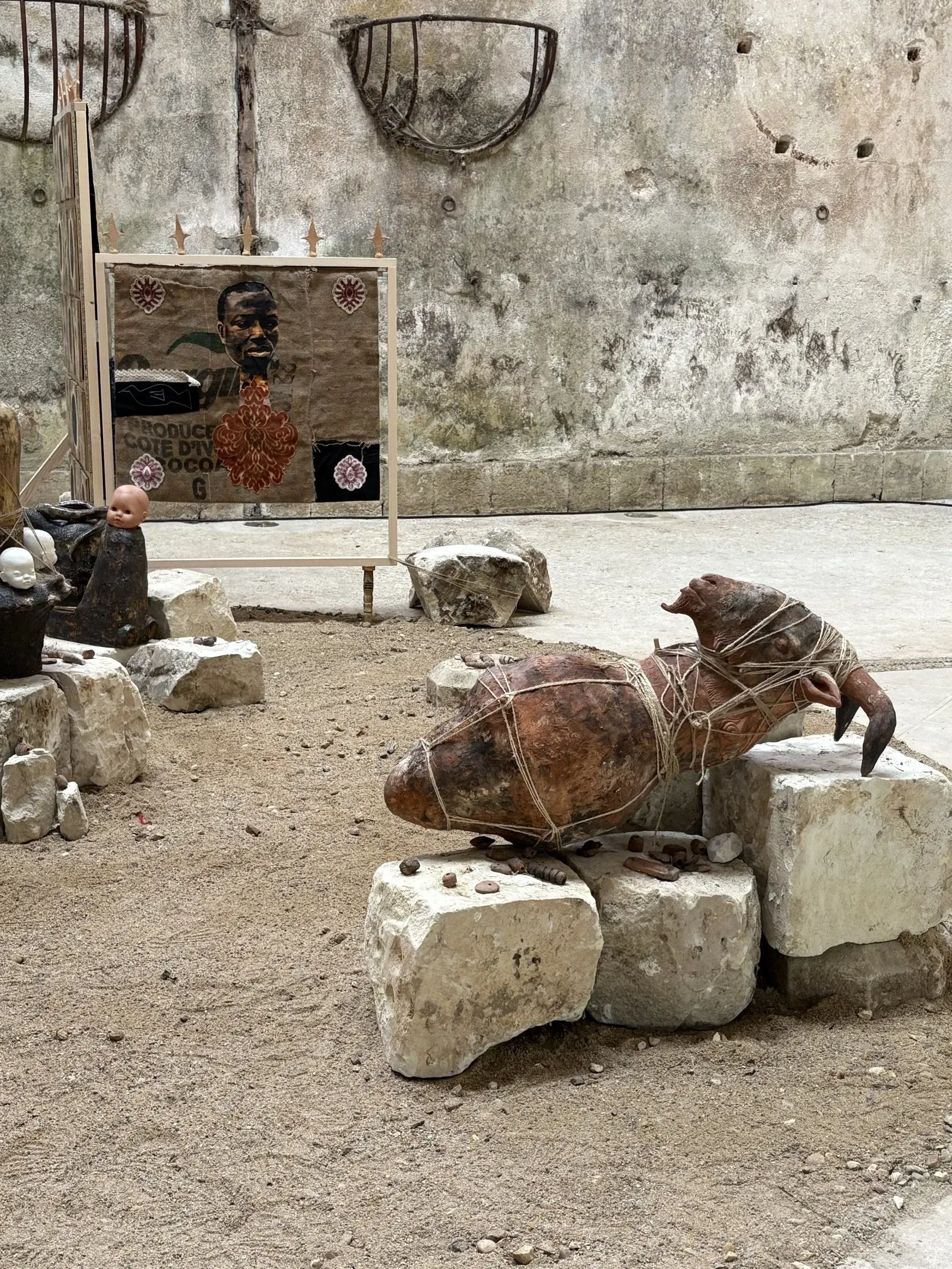 Sculptural installation on stone blocks, with a freestanding mixed-media panel behind it.