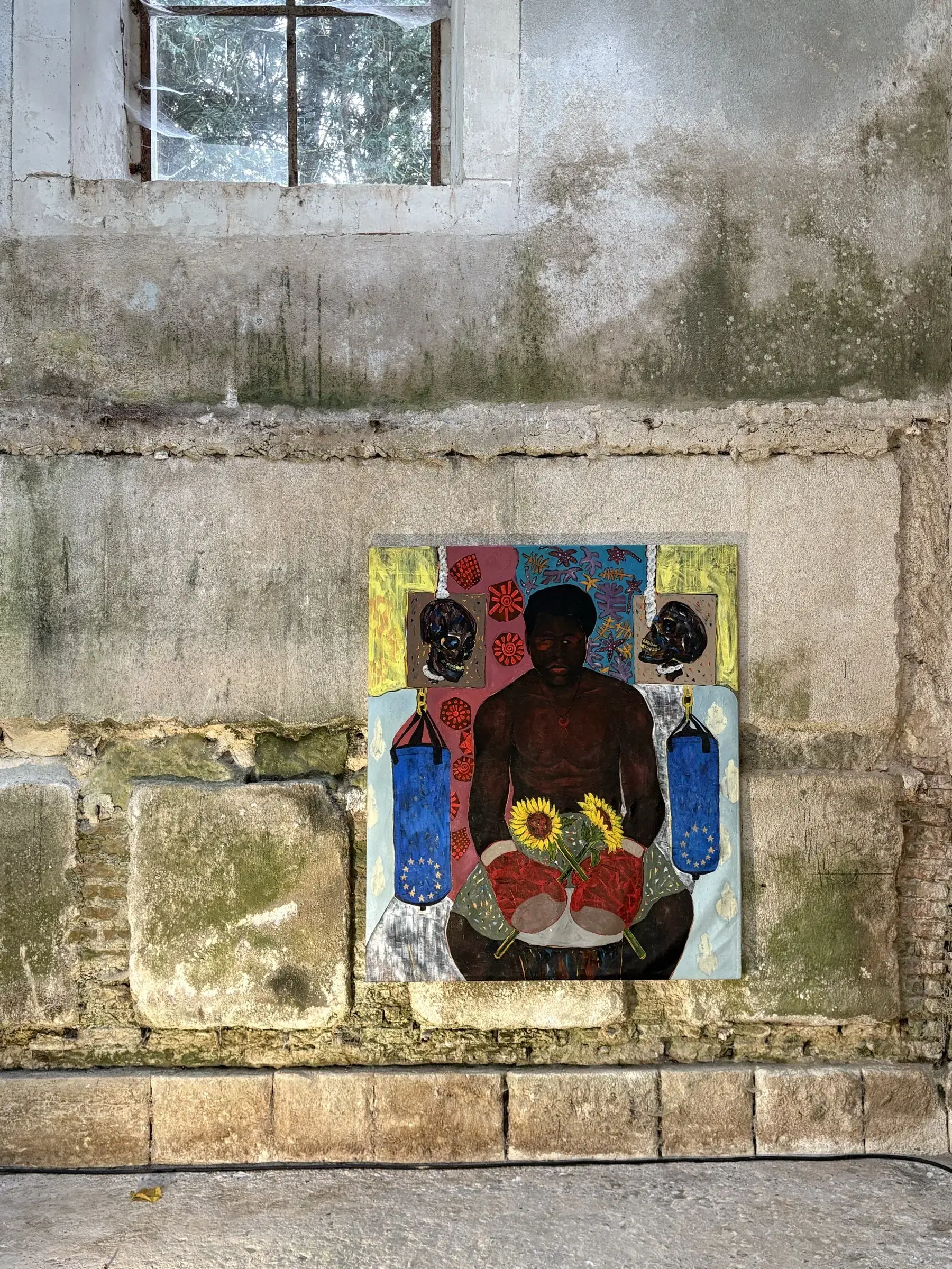 Mixed-media portrait of a seated figure displayed low on a stone wall.