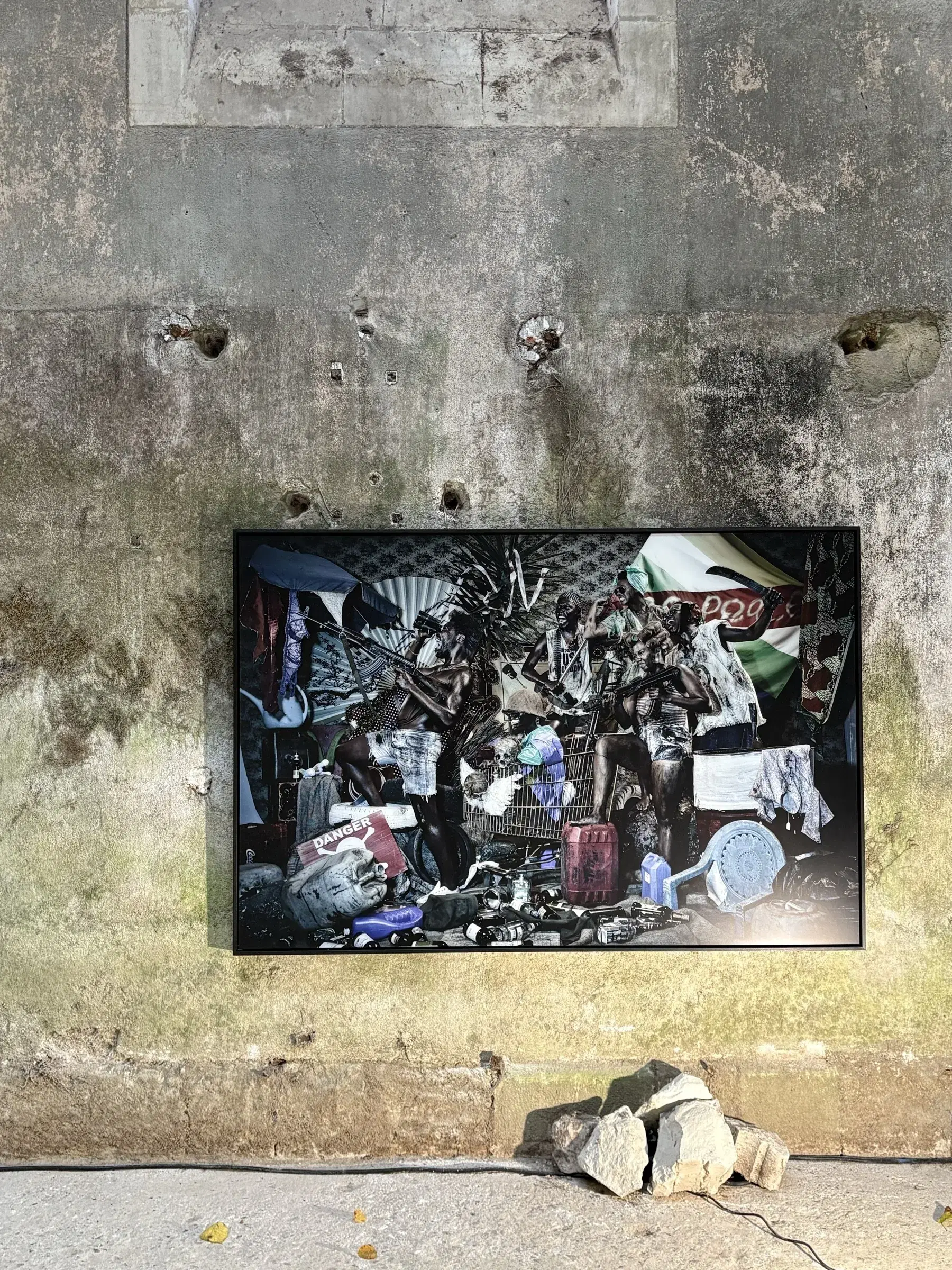 Dark, densely layered mixed-media work displayed on a weathered wall.
