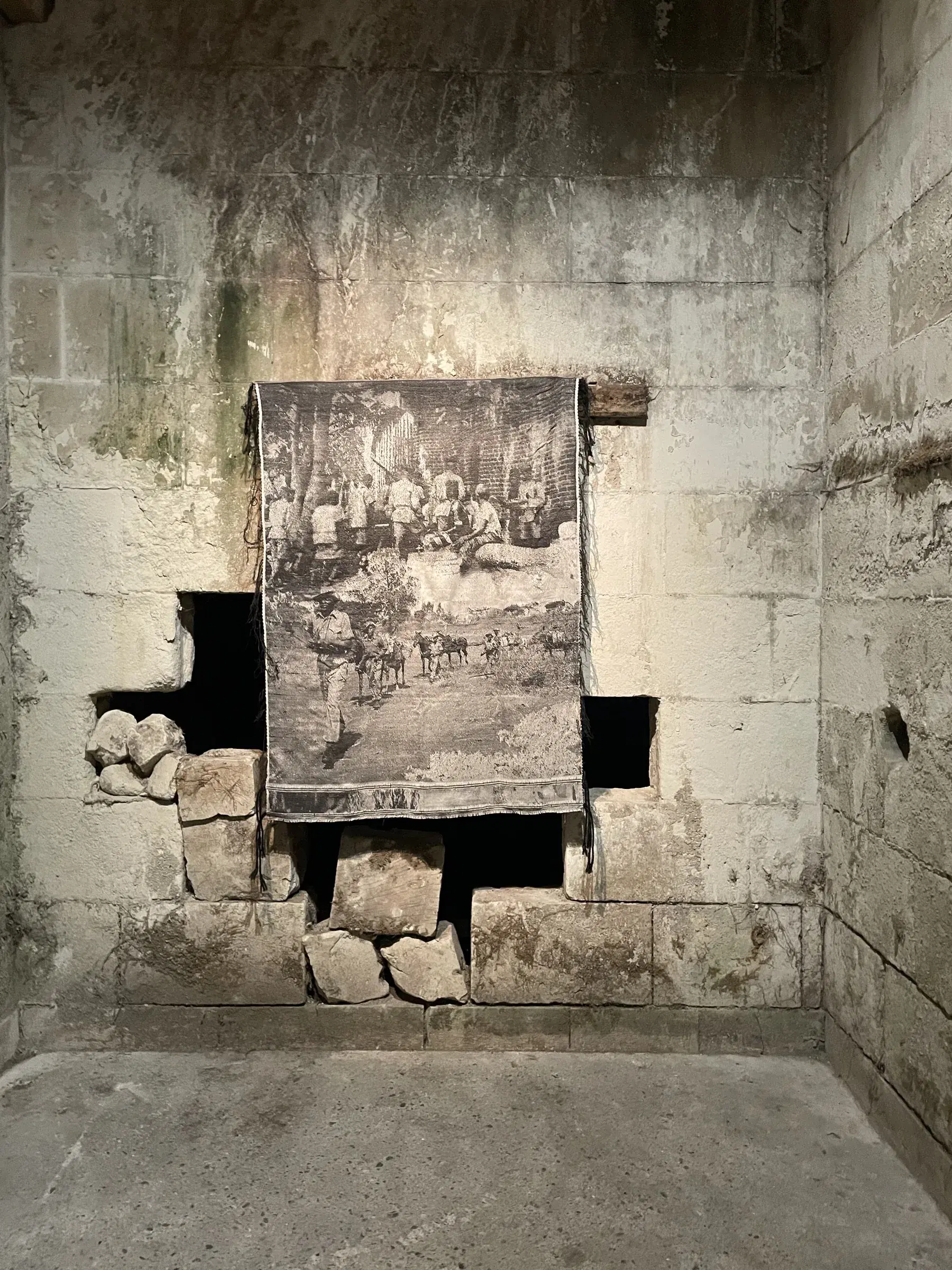 Black-and-white tapestry installed over an opening in a weathered stone wall.