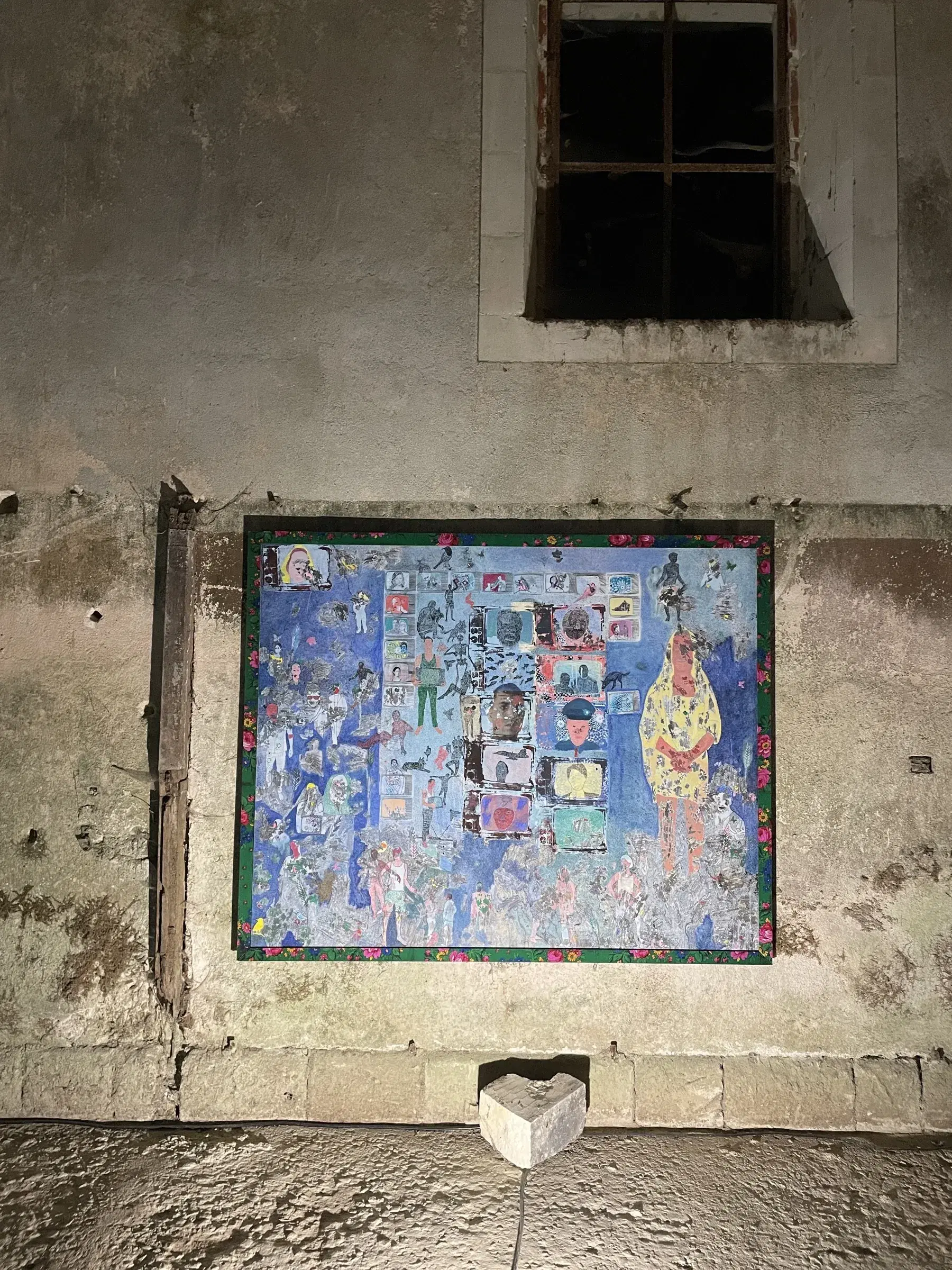 Large blue mixed-media composition installed beneath a dark window in a stone interior.